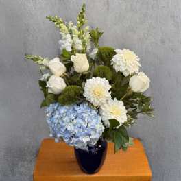 White roses, dahlias, and blue hydrangea in a dark vase