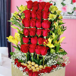Tall box arrangement of red roses with yellow lilies and gold chocolates