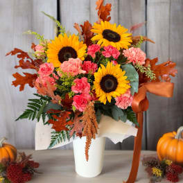 Sunflower and carnation arrangement in a white vase with autumn leaves and ribbon