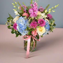 Mixed bouquet of roses, hydrangeas, and pink blooms in a glass vase