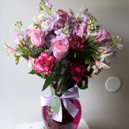 Pink and purple bouquet in a magenta glass vase with a lavender ribbon