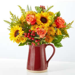 Bouquet of sunflowers, orange roses, and yellow mums in a red pitcher vase