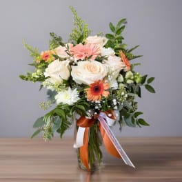 Mixed bouquet of cream roses, peach gerberas, and white blooms in a glass vase