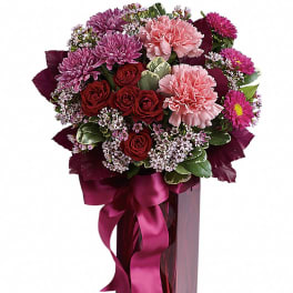 Tall pink vase arrangement with pink carnations, red roses, and purple mums tied with a satin ribbon.