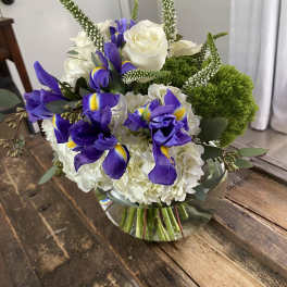 Bouquet of white roses, purple irises, and green accents in a glass vase
