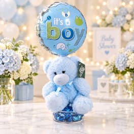 Blue teddy bear with a baby boy balloon and flowers in the background