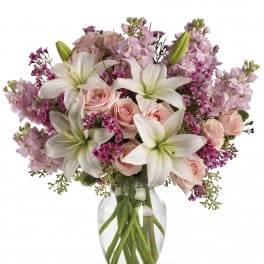 Medium glass vase of white lilies, pale pink roses, and purple flowers