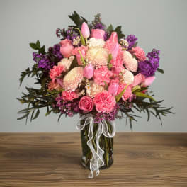 Pink and purple mixed flower bouquet in a glass vase with a white ribbon