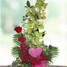 Red roses and green orchids in a vase with a pink heart pick