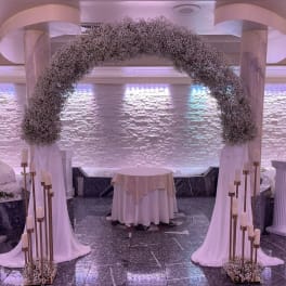Large floral arch with white draping and candle stands in a formal indoor venue