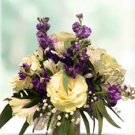 Bouquet of pale yellow roses and purple flowers in a glass vase