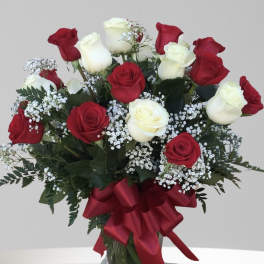 Red and white roses arranged in a glass vase with a red ribbon