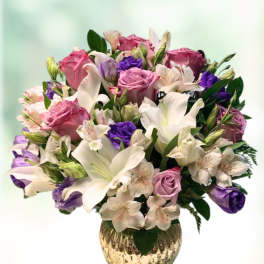 Mixed bouquet of pink roses, white lilies, and purple blooms in a gold vase