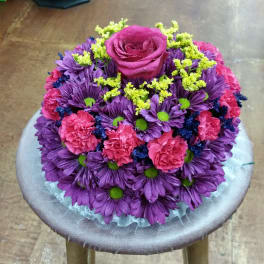 Round bouquet of purple and pink flowers with a magenta rose on top
