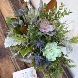 Succulent arrangement with blue thistle-like blooms in a glass vase