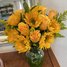 Yellow sunflowers and roses arranged in a glass vase