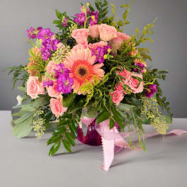 Pink roses and purple flowers arranged in a vase with a peach gerbera daisy