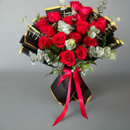 Bouquet of red roses wrapped in black paper with gold trim and a pink ribbon