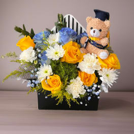 Yellow and blue flower arrangement with a teddy bear in a graduation cap