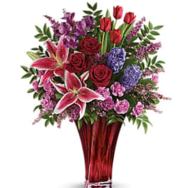 Mixed bouquet of red, pink, and purple flowers in a red glass vase