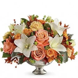 Arrangement of peach roses and white lilies in a silver pedestal vase