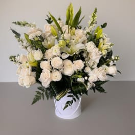 White floral arrangement in a white hatbox with lilies and roses