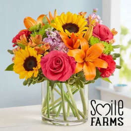 Bright mixed bouquet with sunflowers, orange lilies, and pink roses in a clear glass vase
