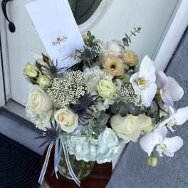 Bouquet of white roses, orchids, and pale hydrangeas in a glass vase