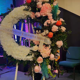 Large crescent-shaped white standing wreath with pink and orange roses on an easel indoors