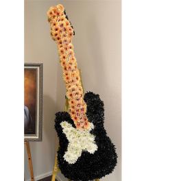 Standing floral arrangement shaped like a guitar with black, peach, and white flowers on an easel.