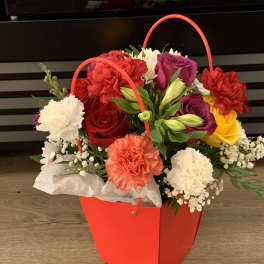 Colorful flower arrangement in a red handled gift bag