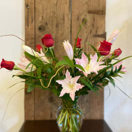 Tall arrangement of red roses and light pink lilies in a clear glass vase