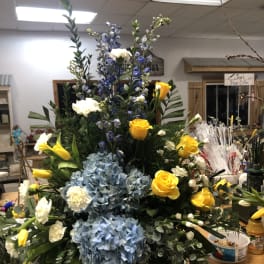 Large floral arrangement with blue hydrangeas, yellow roses, and white blooms