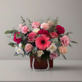 Mixed pink and white flower arrangement in a wicker basket with pearl handle