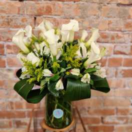 White calla lilies and small white blooms in a glass vase