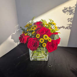Red roses and yellow button flowers in a square glass vase