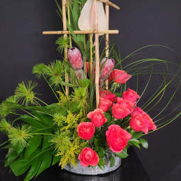 Pink roses and tropical flowers arranged in a bamboo frame with a white vase