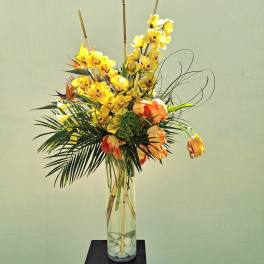 Tall yellow orchid arrangement in a clear glass vase with orange blooms