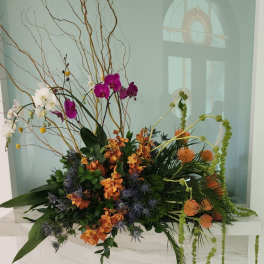 Tall floral arrangement with orchids, orange blooms, and twisting branches