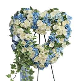 Heart-shaped floral wreath with white and blue flowers on a stand
