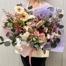 Large pastel bouquet with roses, lilies, and gerbera daisies wrapped in pink and lavender paper