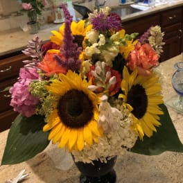 Colorful bouquet with sunflowers, hydrangeas, and snapdragons in a black vase