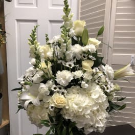 White floral arrangement in a glass vase with roses, lilies, and hydrangeas