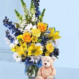 Mixed bouquet in a glass vase with a teddy bear beside it