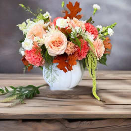 Peach and coral floral arrangement in a white vase with autumn leaves