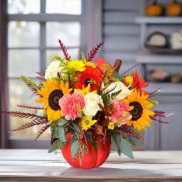 Autumn bouquet with sunflowers, roses, carnations, and gerbera daisies in a pumpkin vase