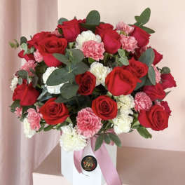 Red roses and pink carnations in a white box with a pink ribbon