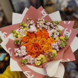 Bouquet of orange roses and pale pink flowers wrapped in pink and white paper