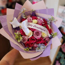 Bouquet of pink, red, and cream roses wrapped in lavender paper with a white ribbon