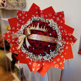 Bouquet of red roses with baby's breath, a gold ribbon, and a crown topper